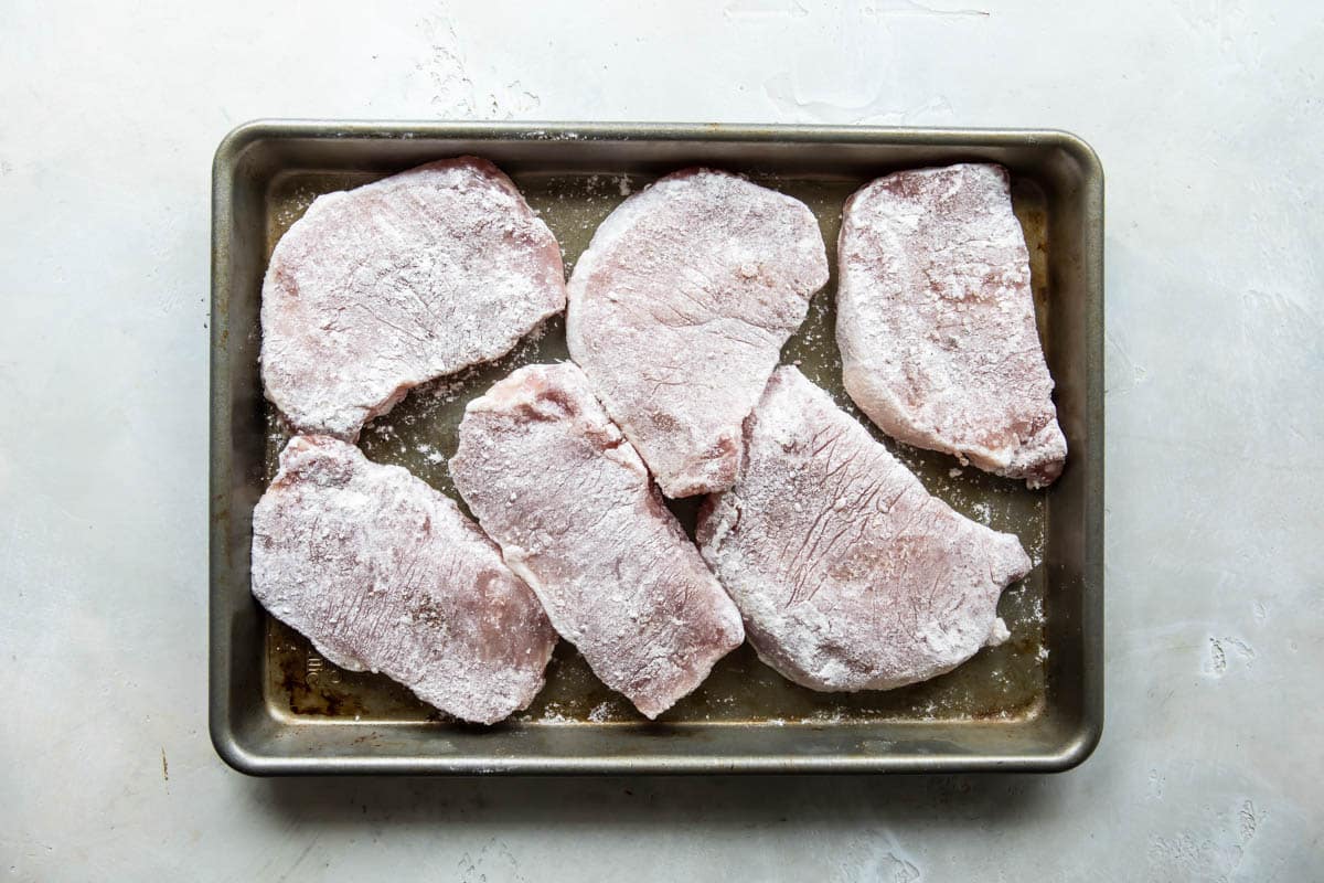 Flour coated pork cutlets in a baking pan.