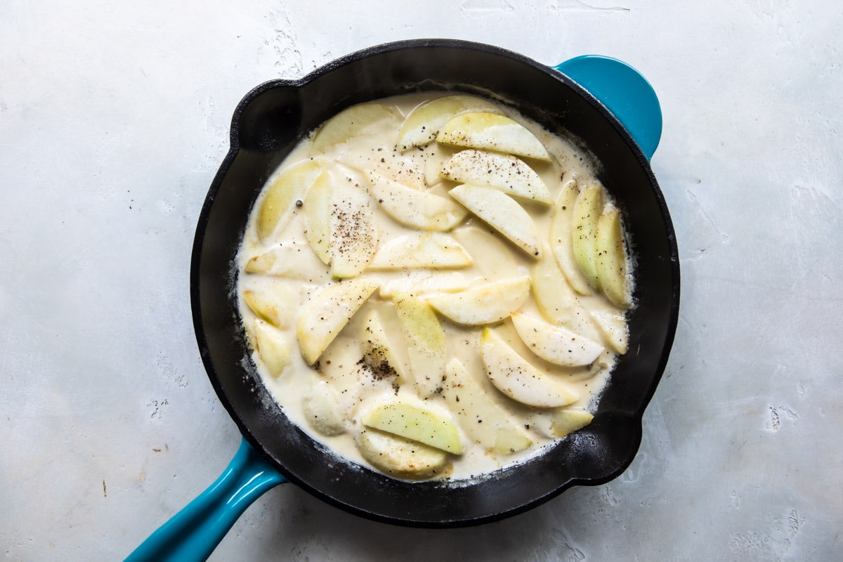 Apples cooking in a cream sauce in a skillet.
