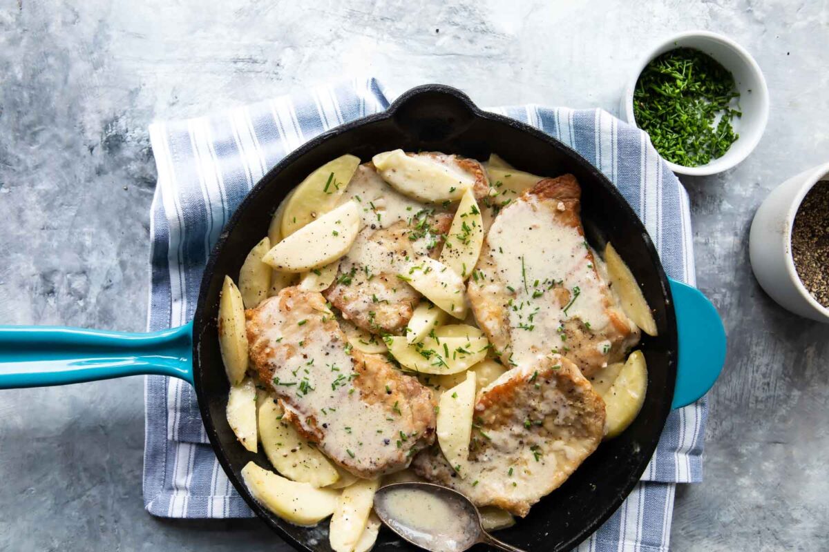 Pork cutlets with apples in a skillet with spoon.