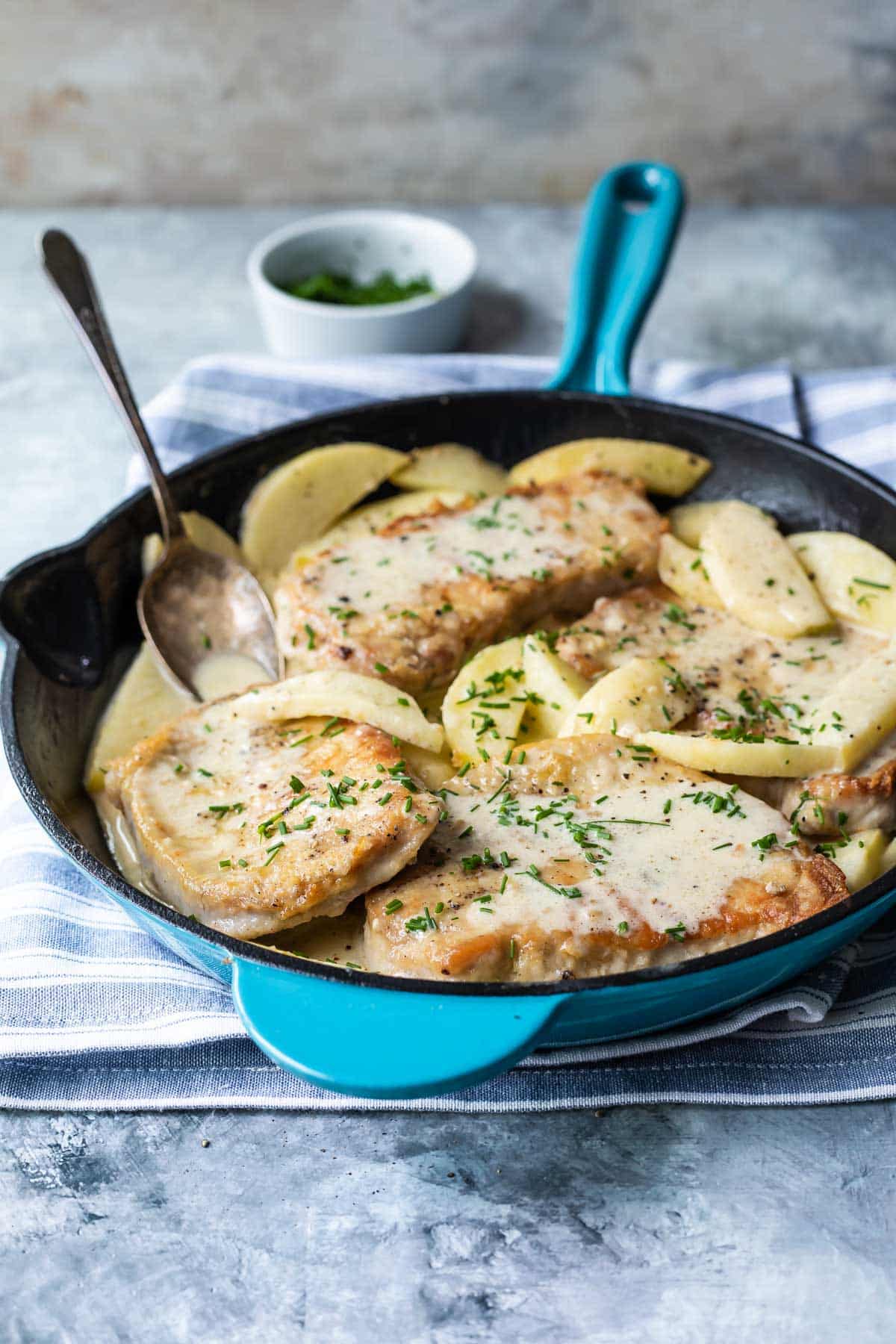 A cast iron skillet with pork cutlets and apples.