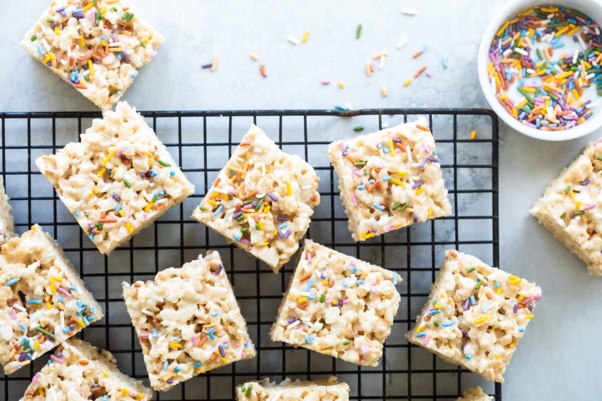 Rice Krispie treats on cooling rack next to a cup of sprinkles.