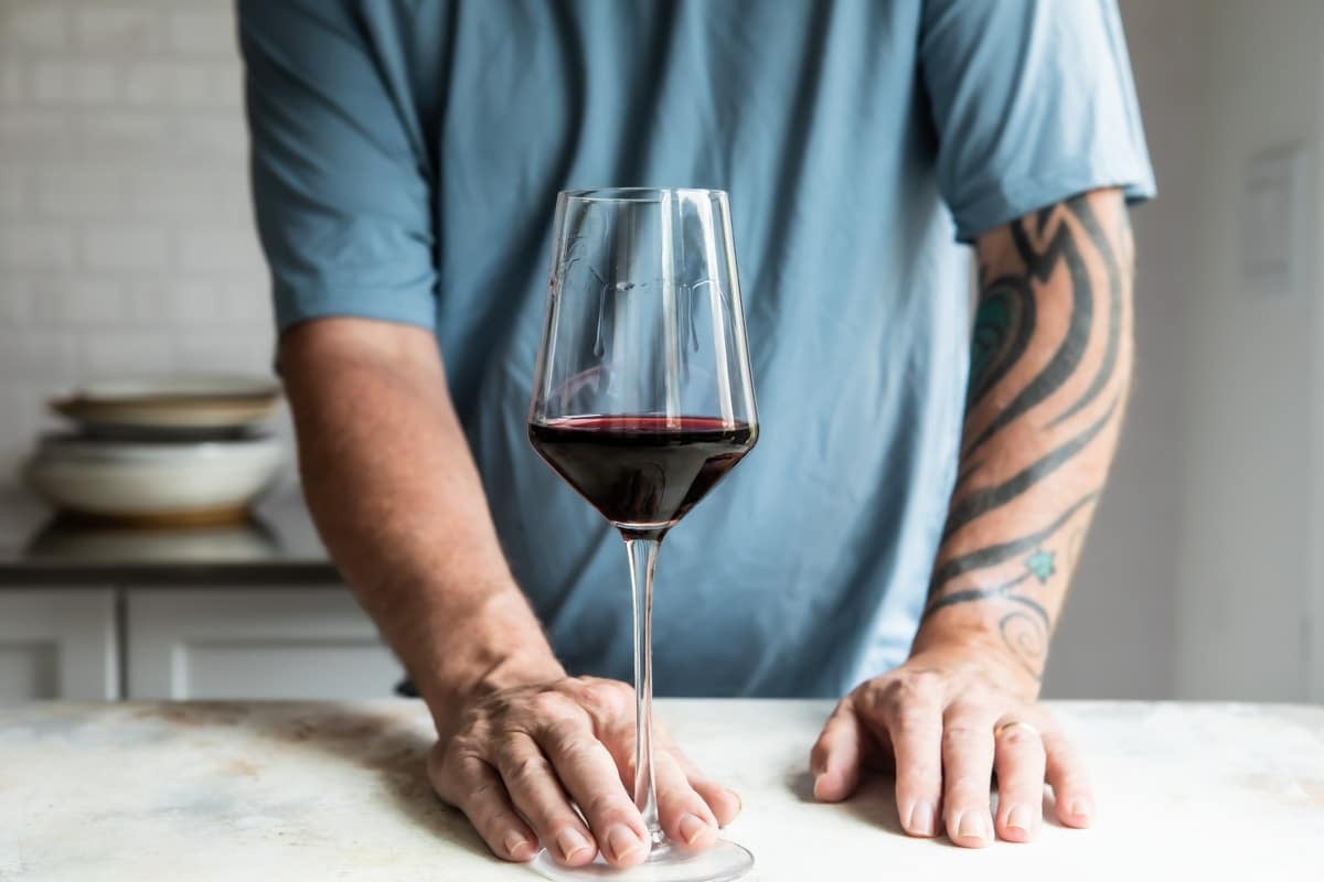 Someone holding a glass of red wine on a countertop.