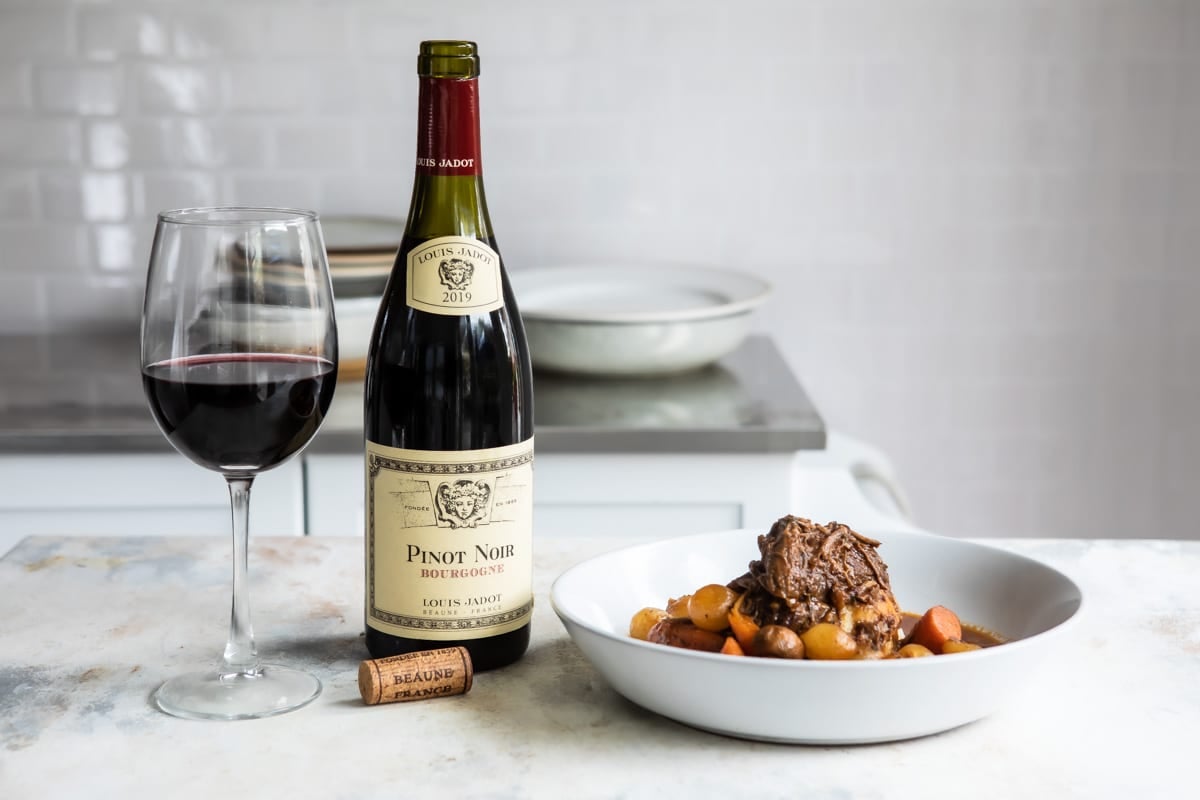 A glass and bottle of Pinot Noir next to a bowl of beef bourguignon.