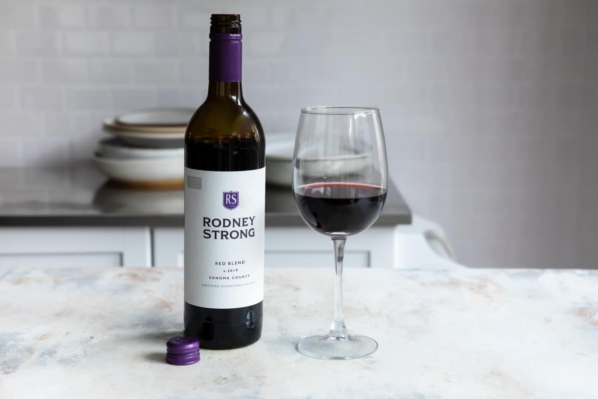 A red wine glass on a counter next to a bottle of Rodney Strong.
