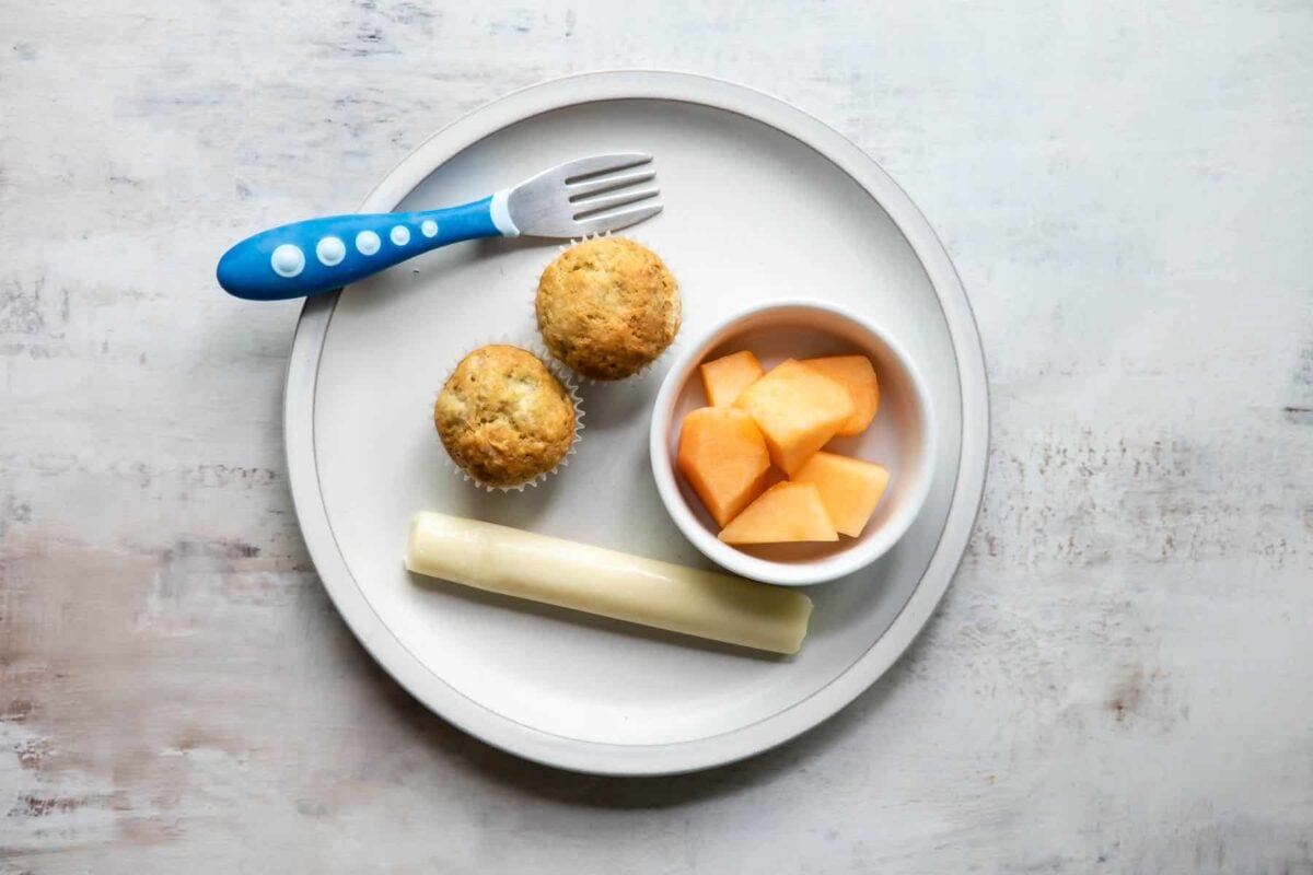 A plate with mini banana muffins, cantaloupe, and string cheese on it.
