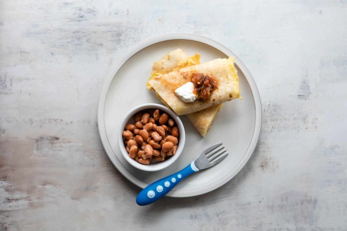 A plate with an egg burrito and a side of beans.