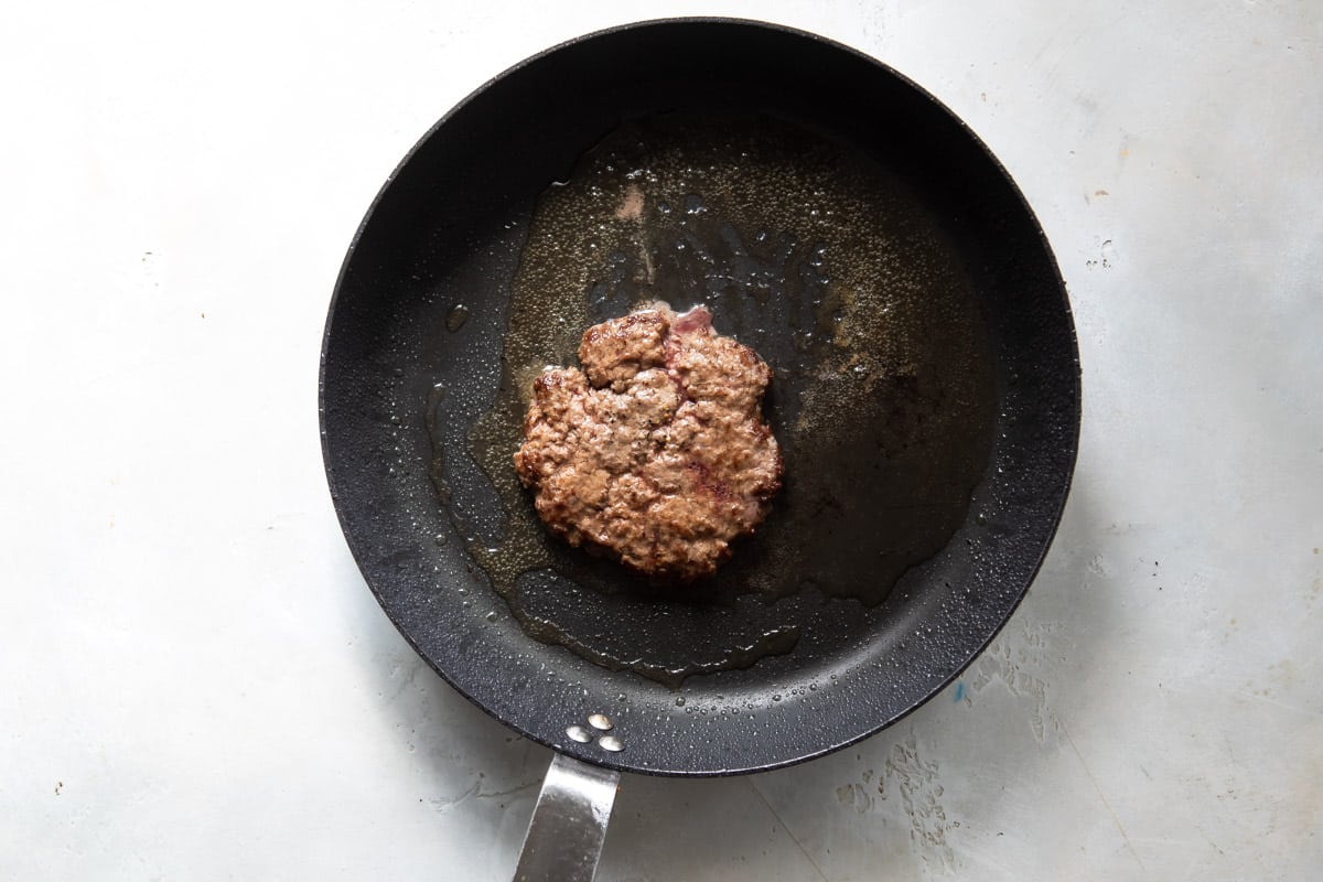 A smashed burger patty in a skillet.