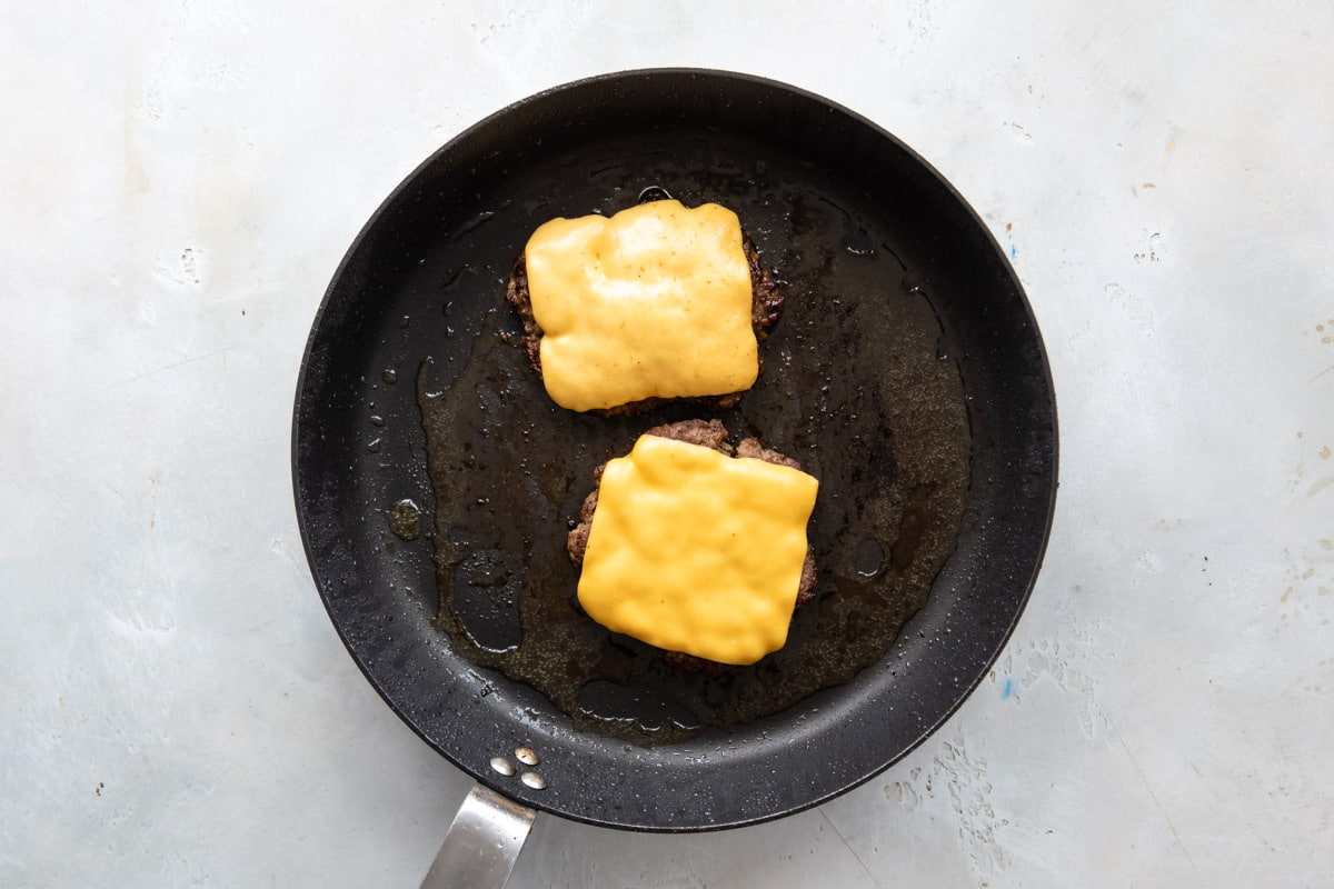Two cheeseburgers cooking in a skillet.