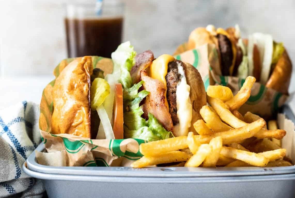 Bacon cheeseburgers wrapped in paper with a pile of fries nearby.