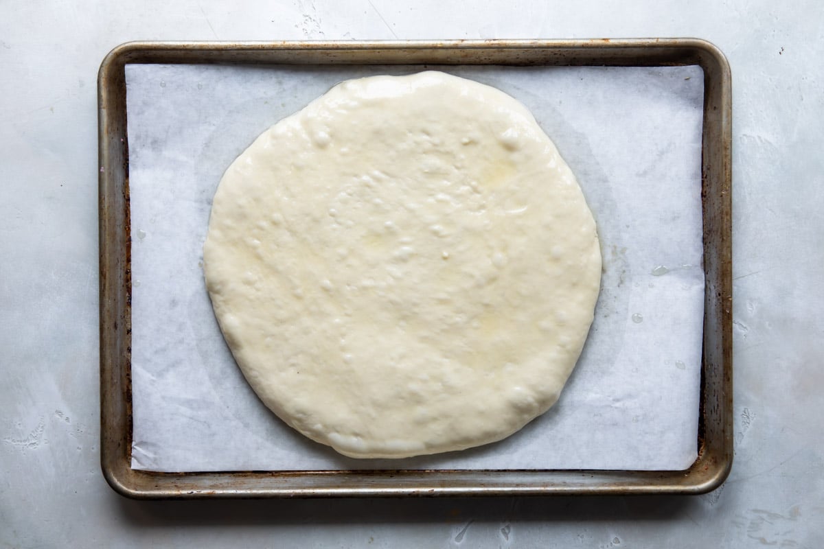 Focaccia bread dough spread out on a baking sheet.