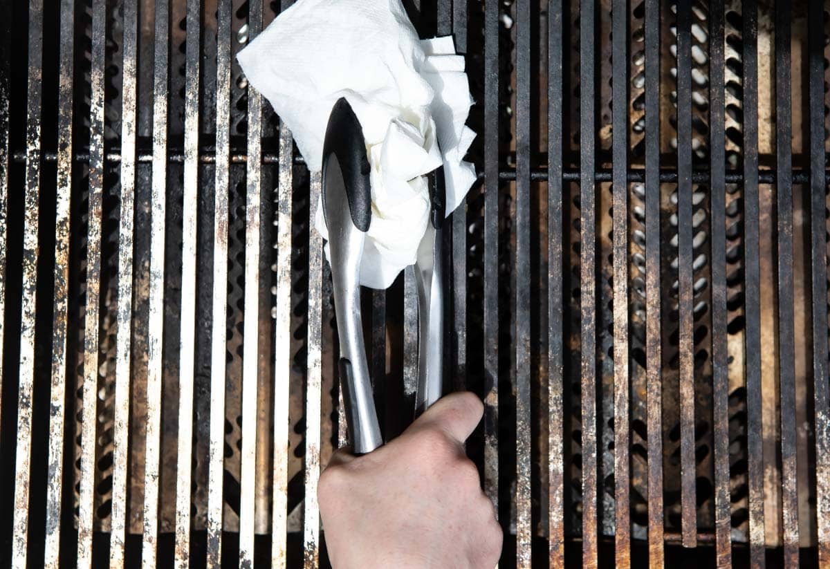 Someone holding a paper towel in tongs over a grill.