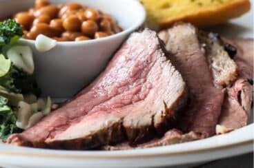 A plate of Santa Maria barbecue with tri-tip, salad, beans, and garlic toast.