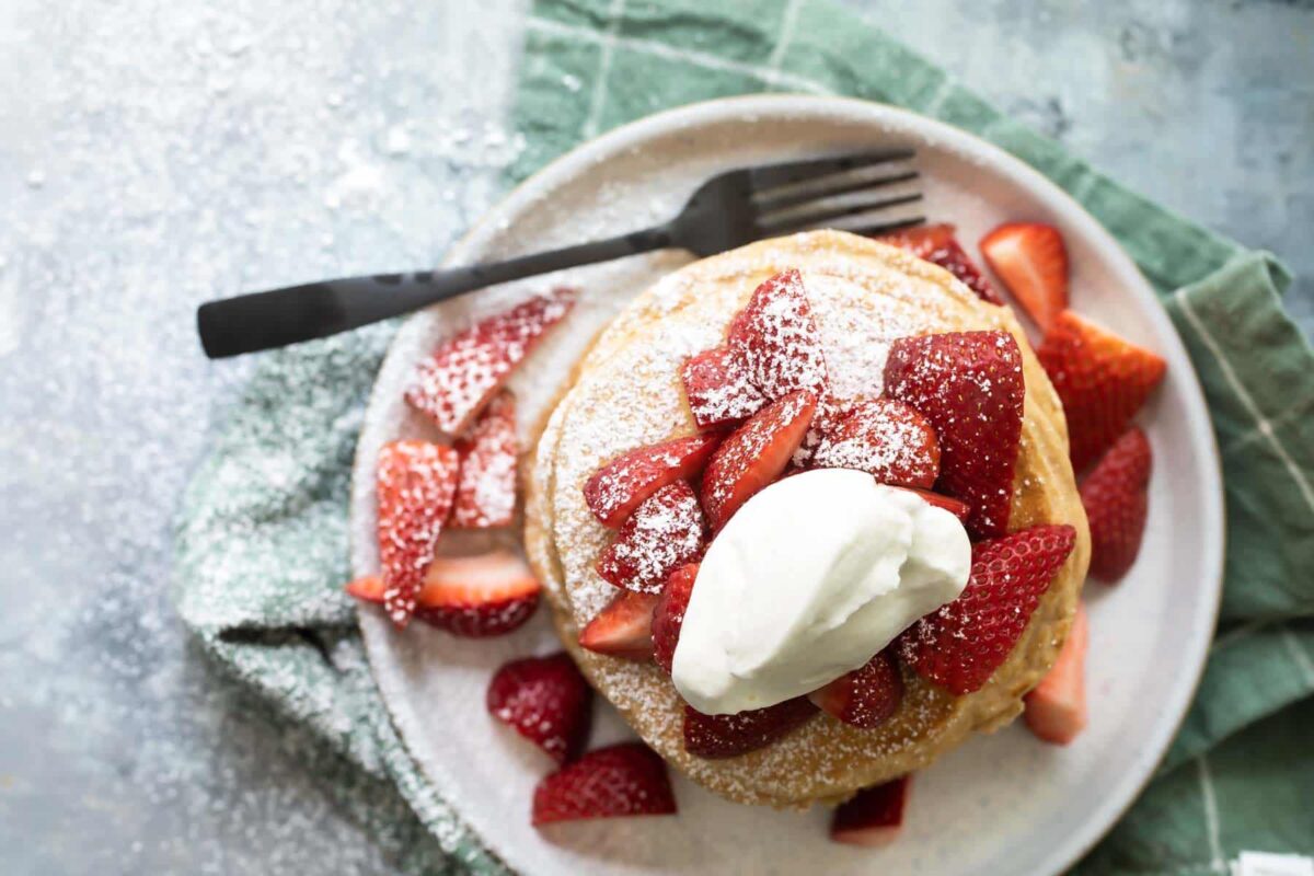 A stack of pancakes with strawberries and whipped cream.