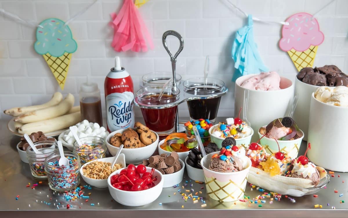 Two ice cream sundaes and a banana split surrounded by various ice cream toppings.