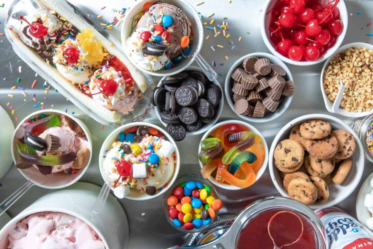 Two ice cream sundaes and a banana split surrounded by various ice cream toppings.