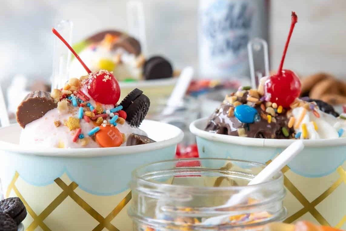 Two ice cream sundaes surrounded by various ice cream toppings.