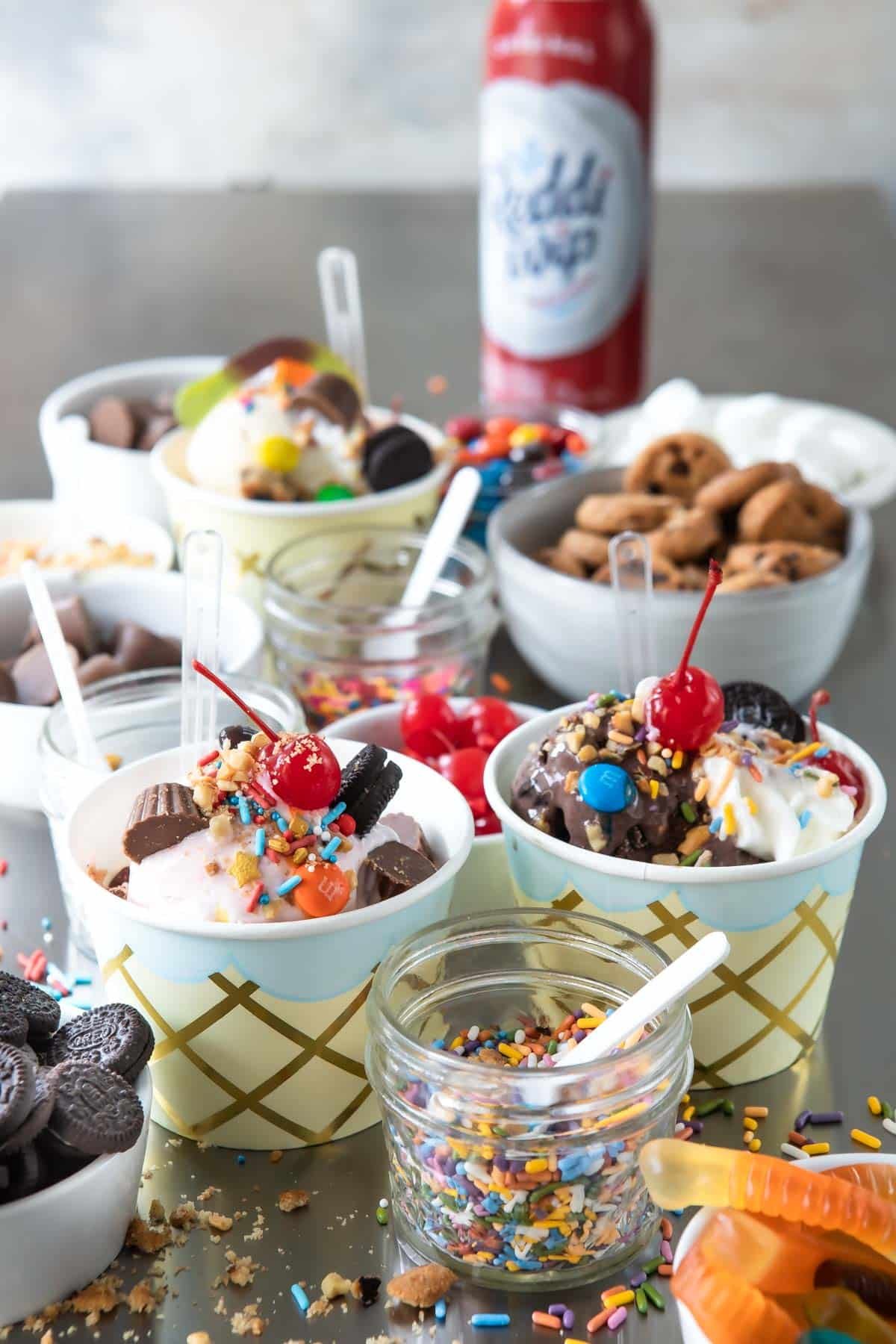 Two ice cream sundaes surrounded by various ice cream toppings.