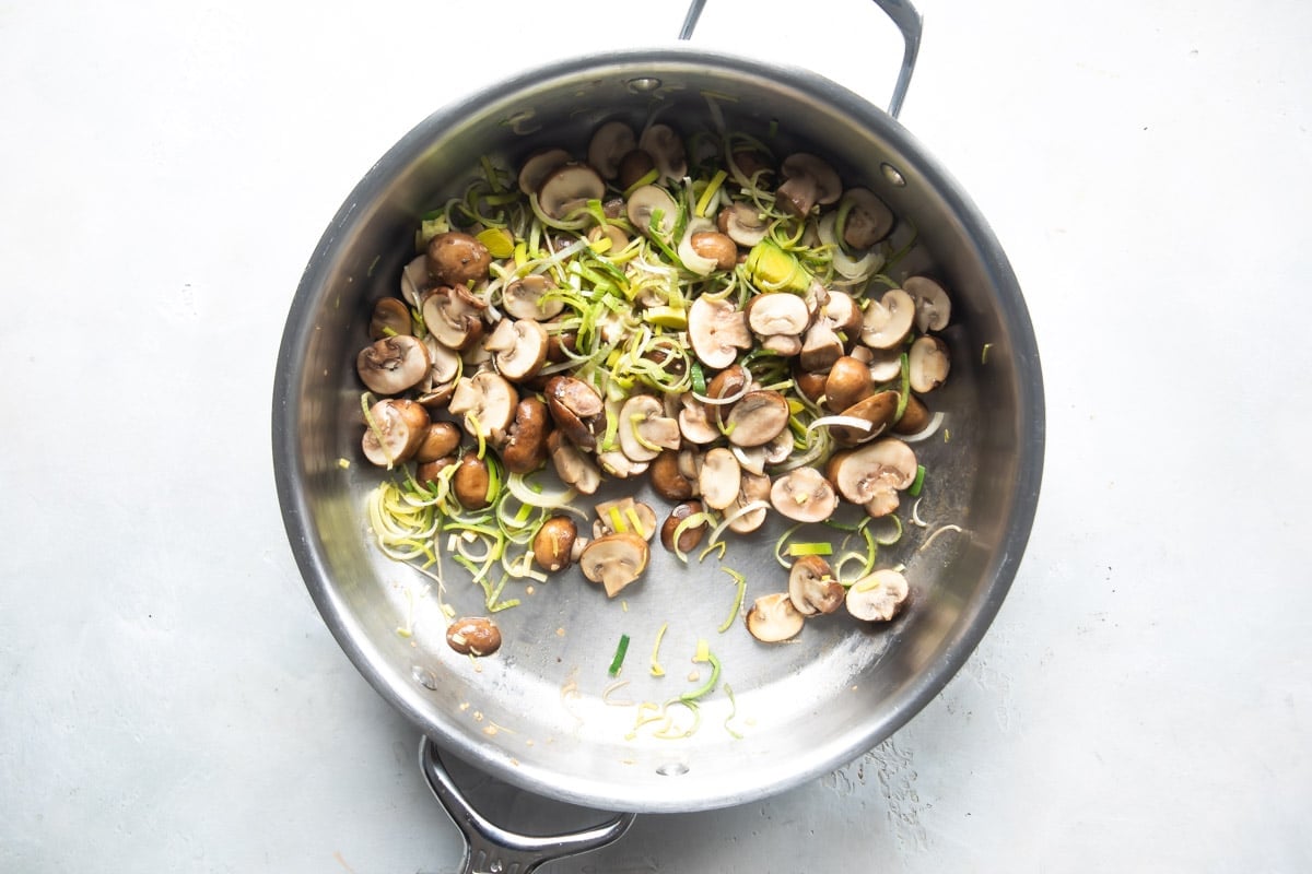 Mushrooms and leeks being cooked in a silver skillet.
