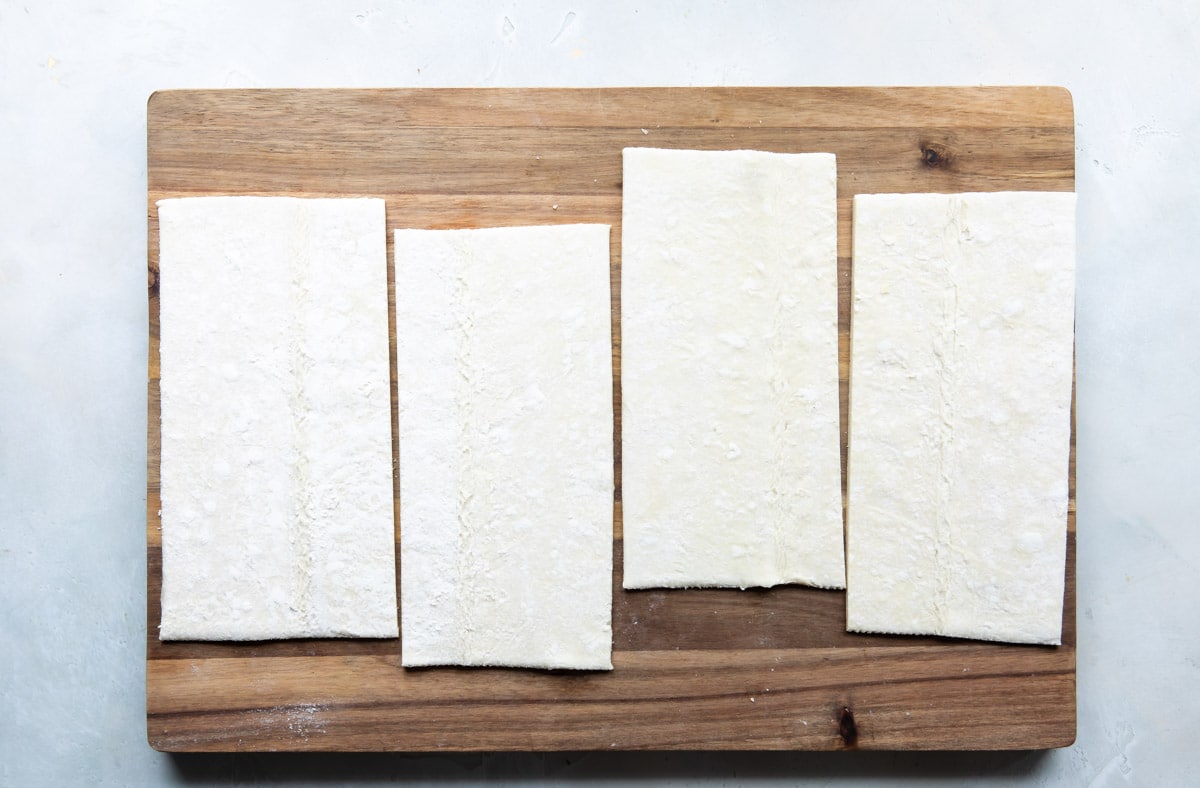 Four pieces of puff pastry laid out flat on a wooden cutting board.
