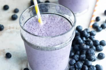 2 glasses of blueberry smoothies next to fresh blueberries.