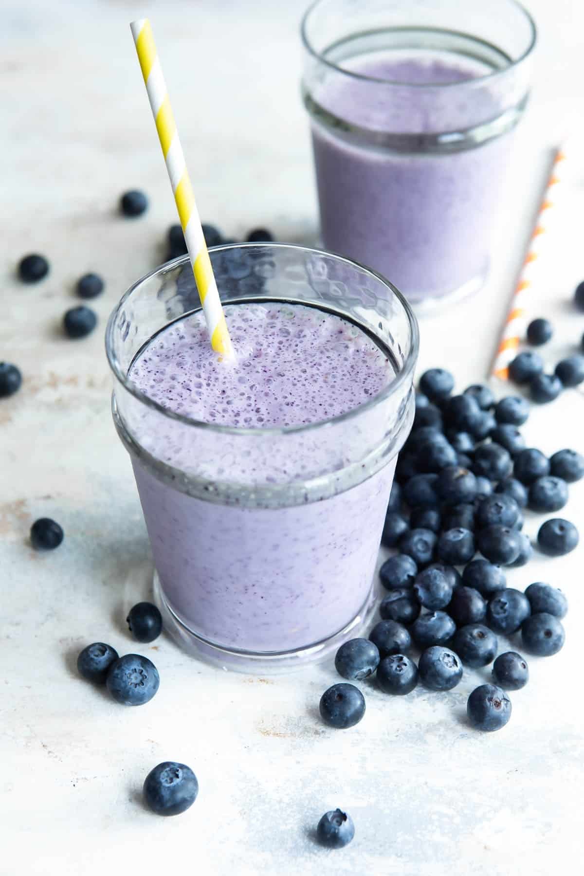 2 glasses of blueberry smoothies next to fresh blueberries.