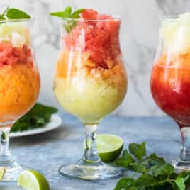 Three granitas on a counter surrounded by garnishes.