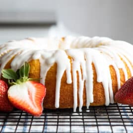 A lemon bundt cake on a cooling rack surrounded by strawberries.