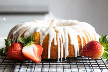A lemon bundt cake on a cooling rack surrounded by strawberries.