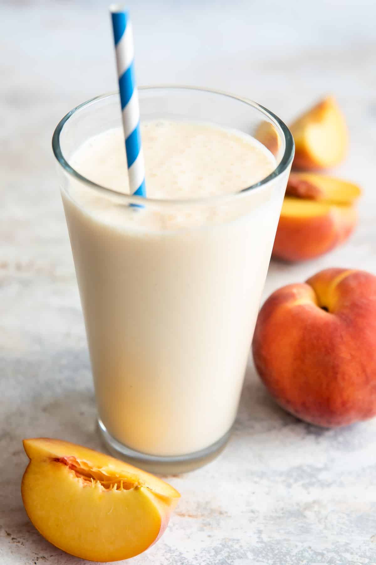 A glass of peach smoothie next to fresh peaches on a counter.