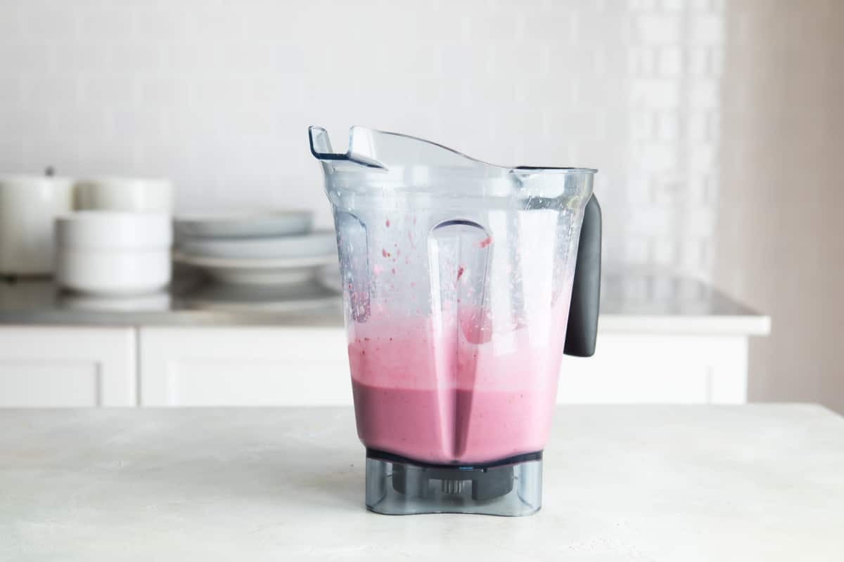 A blender with raspberry smoothie ingredients.
