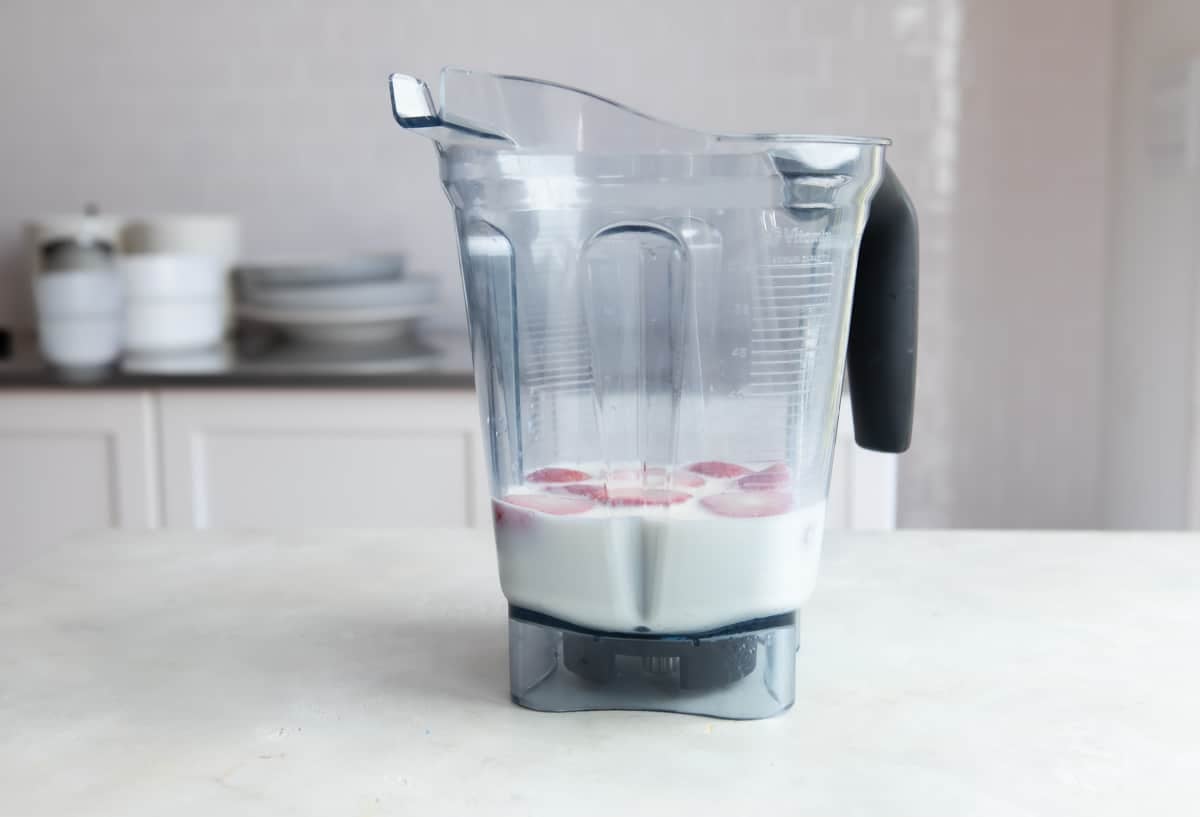 A blender with strawberry smoothie ingredients inside.