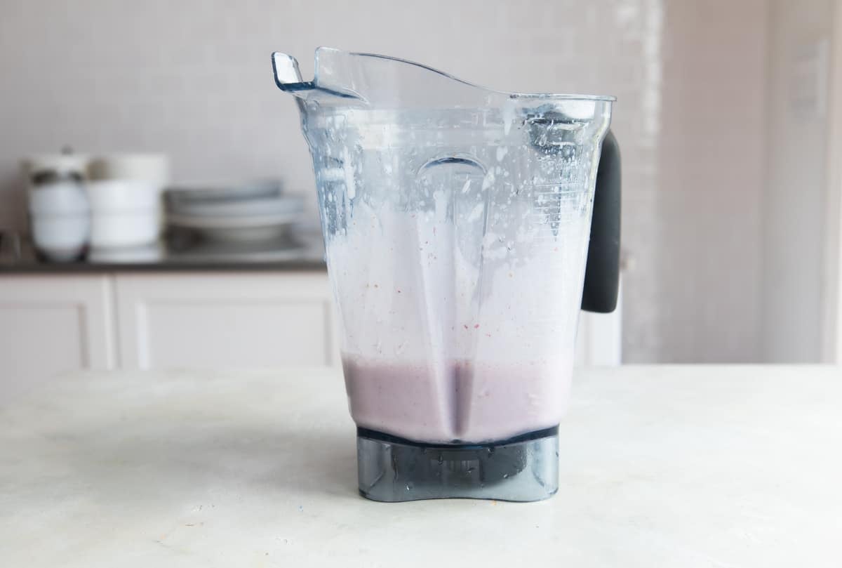 A blender with strawberry smoothie ingredients inside.