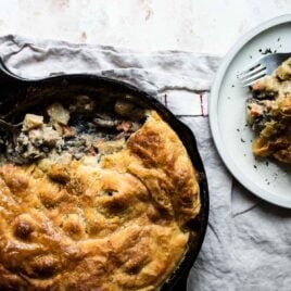 Vegetable pot pie in a cast iron skillet next to a plate with a serving of vegetable pot pie.