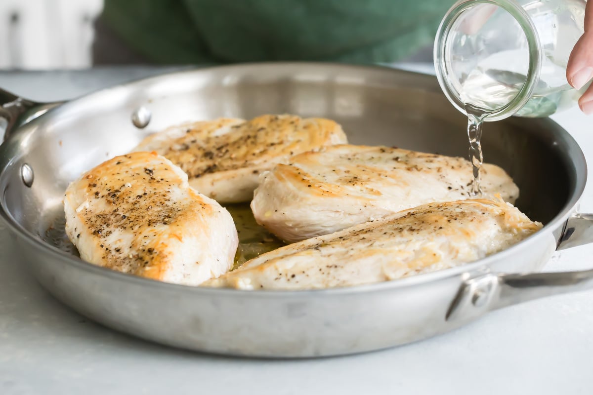 Adding water to a skillet of chicken breasts to poach them.