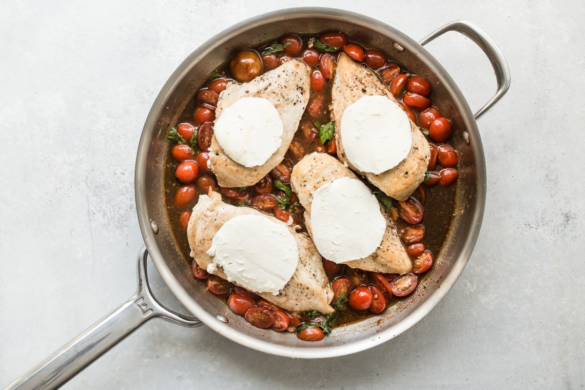 A skillet of Caprese Chicken, the mozzrella cheese not yet melted over the chicken.