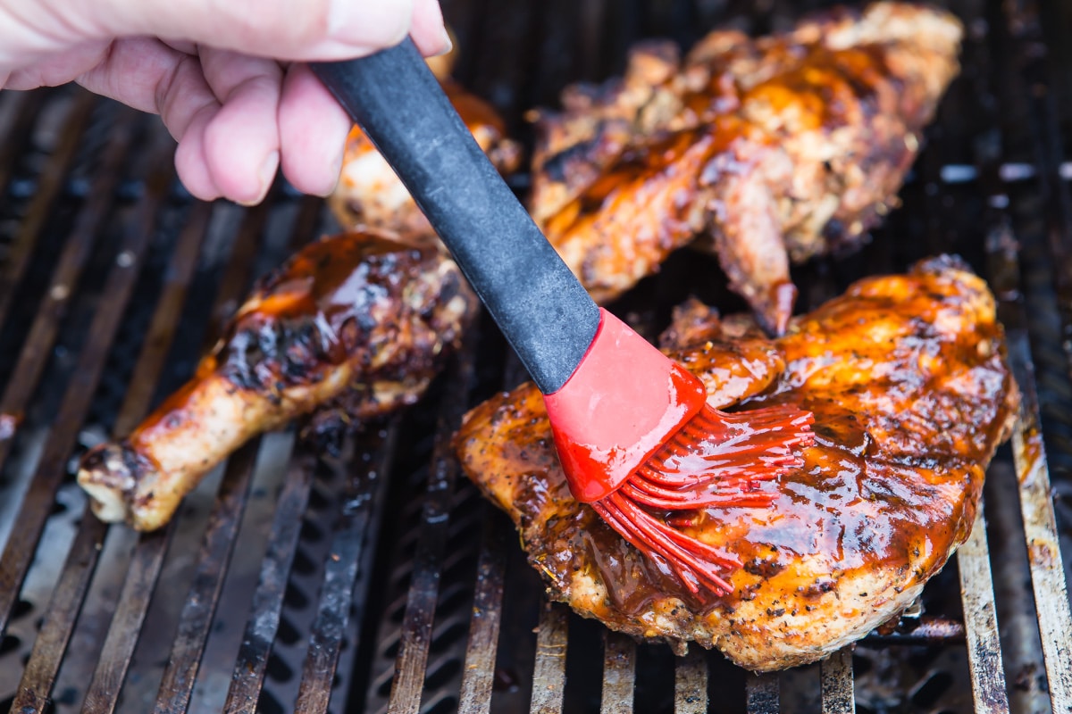 Brushing chicken on a grill with barbecue sauce.