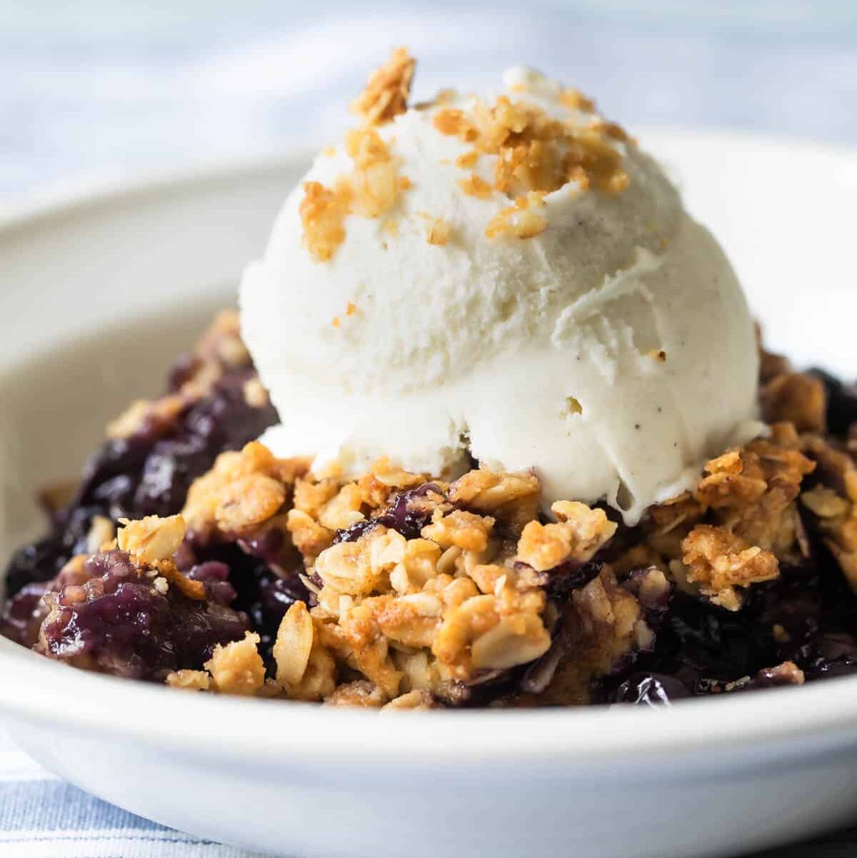 A bowl of blueberry crisp with a scoop of ice cream on top.