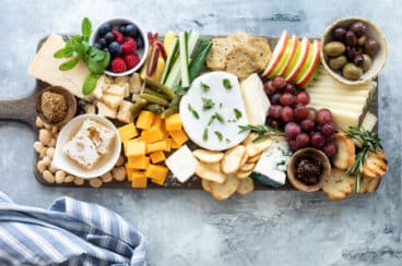 A cheese board filled with fruits, vegetables, nuts, crackers, and cheese.