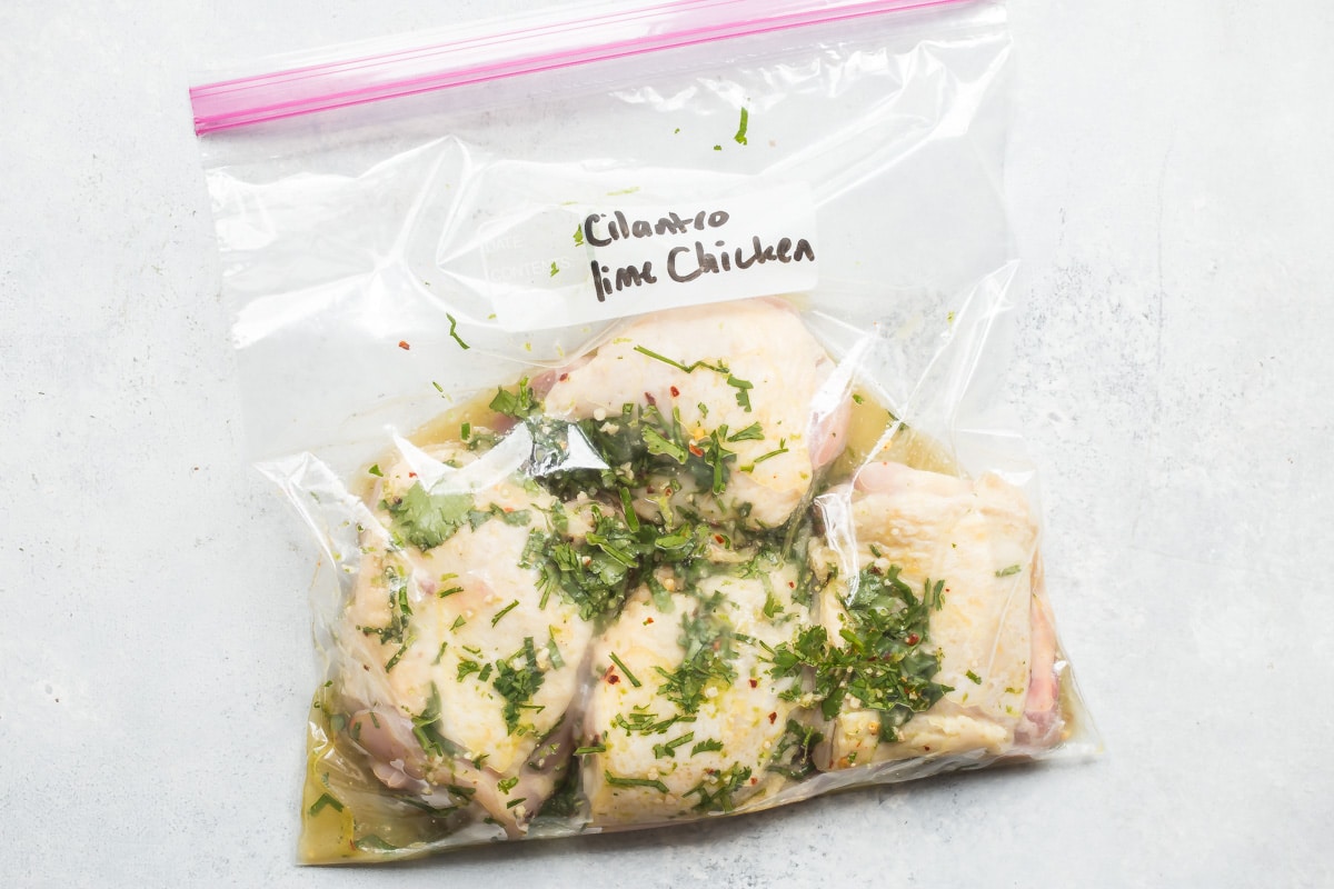 Raw chicken thighs in a plastic bag of cilantro-lime marinade.