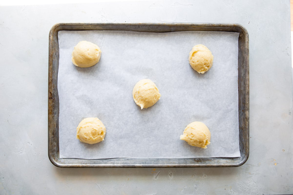 Pate-choux dough for cream puffs portioned out on a baking sheet.