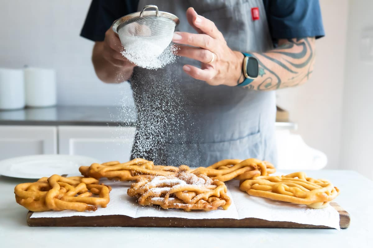 Dusting powered sugar over fried funnel cakes.