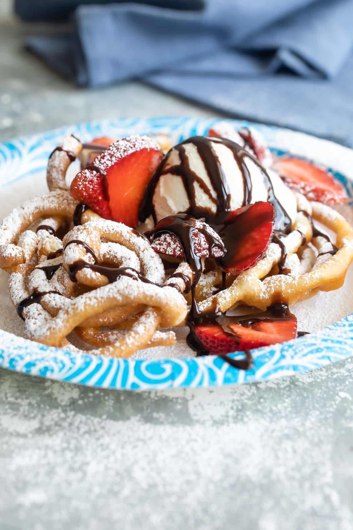 Funnel cakes topped with ice cream, chocolate sauce, and strawberries.