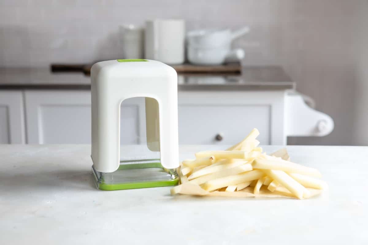 Cut french fries next to a french fry cutter.