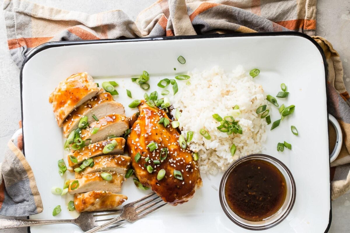 Honey garlic chicken with white rice and a clear bowl of sauce on a white serving platter.