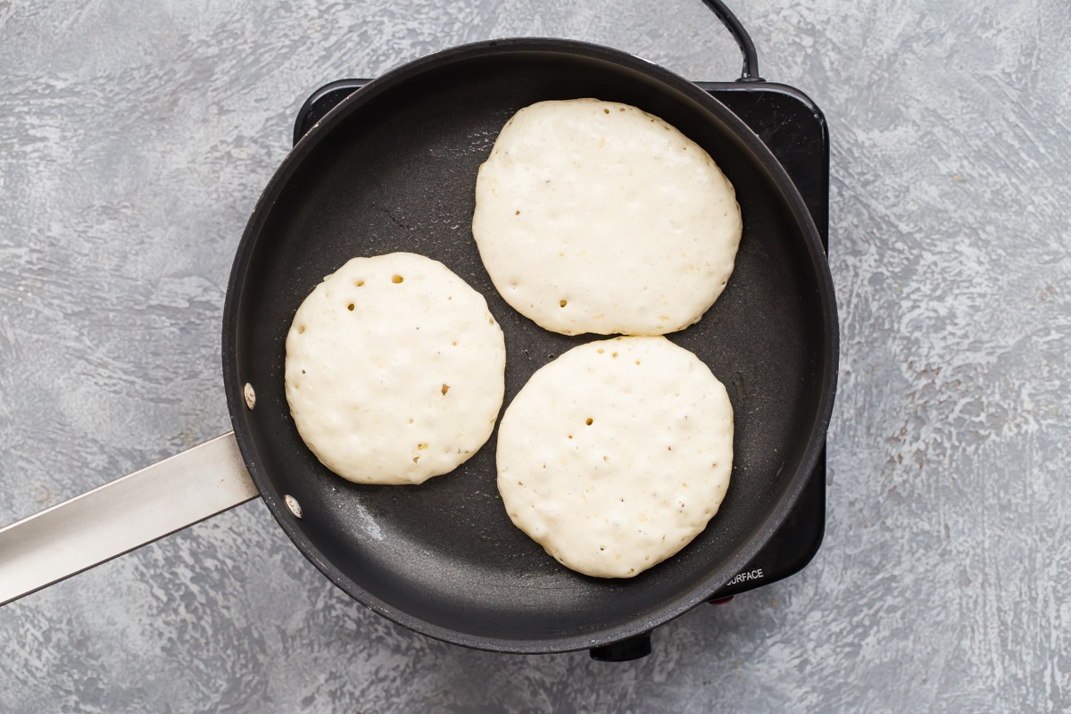 A skillet with 3 lemon ricotta pancakes in it.