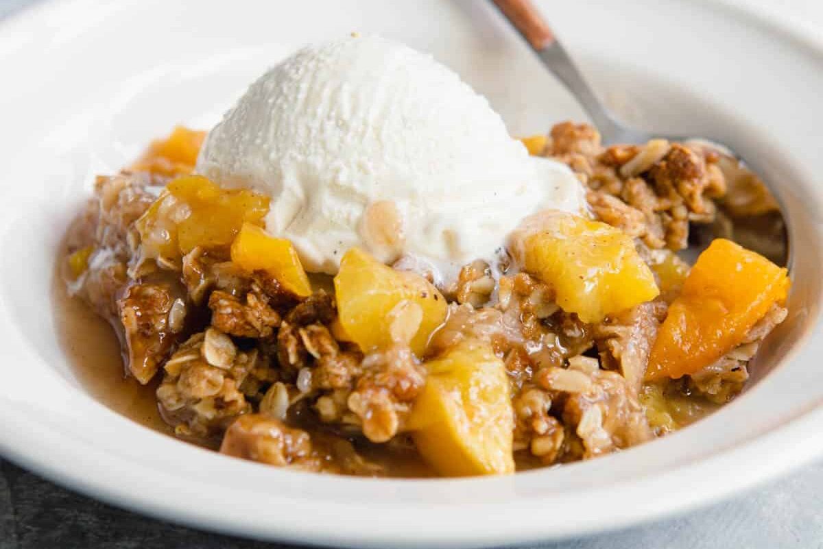 A bowl of Peach Crisp with a scoop of vanilla ice cream on top.