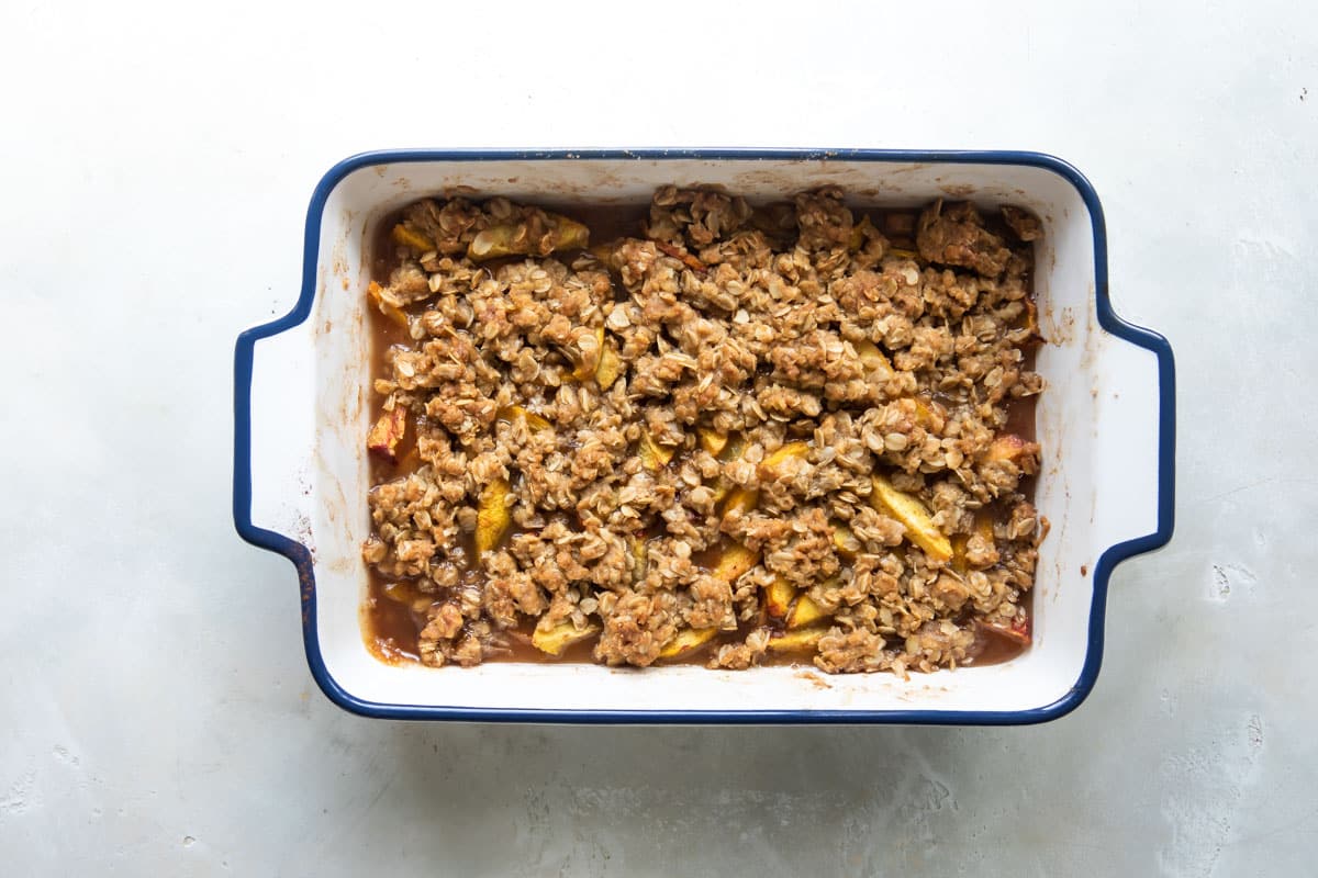 A fully baked peach crisp in a white baking dish.