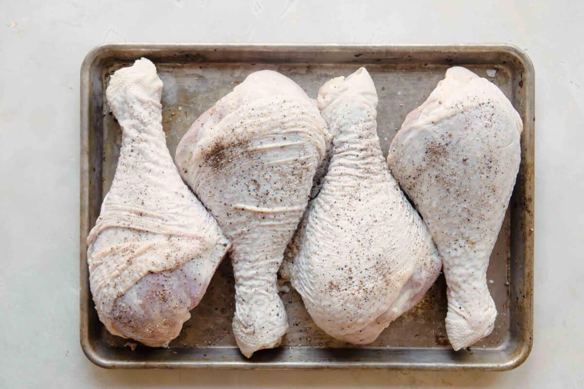 Raw turkey legs on a metal baking sheet.