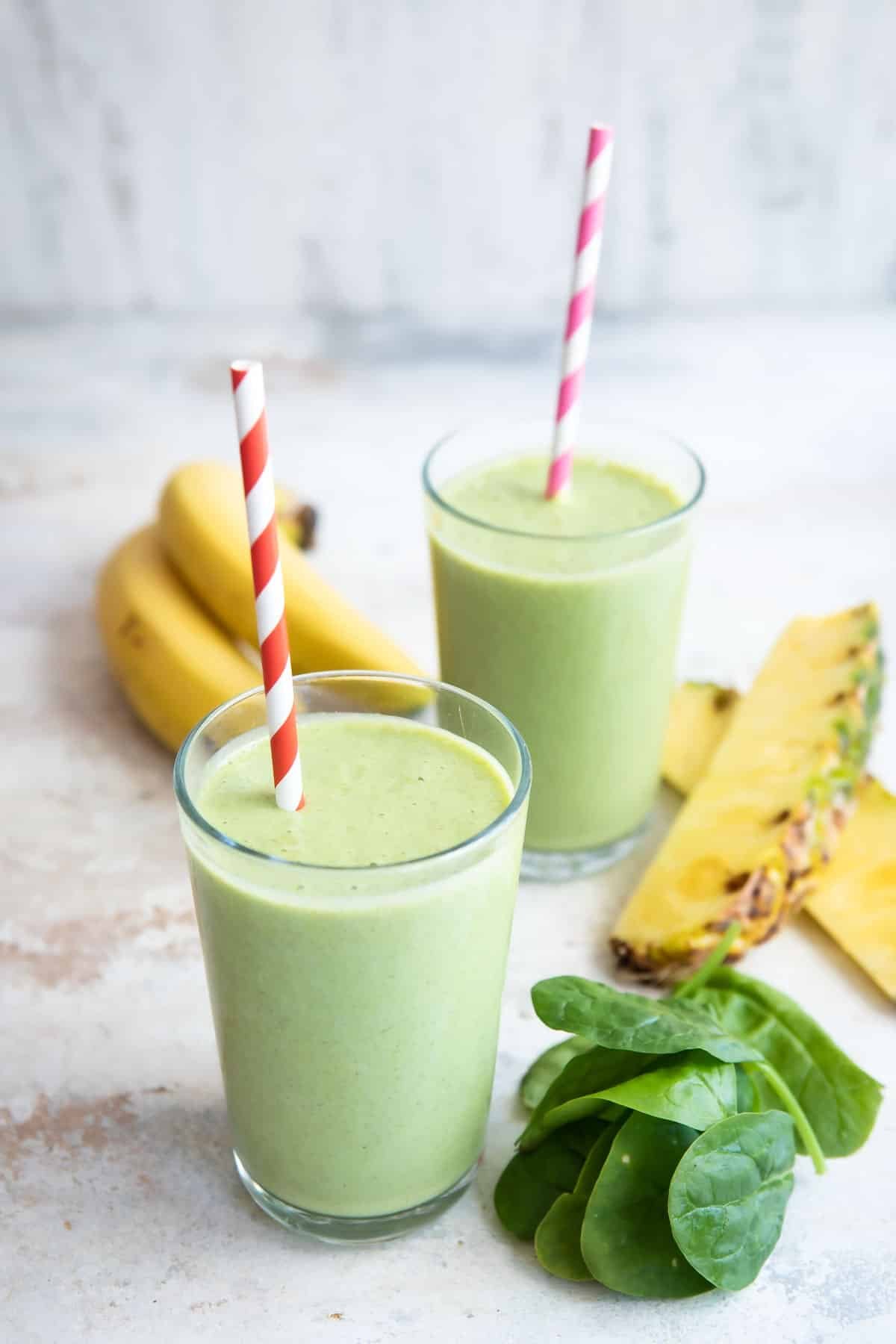 2 glasses of Spinach Smoothie with ingredients nearby.