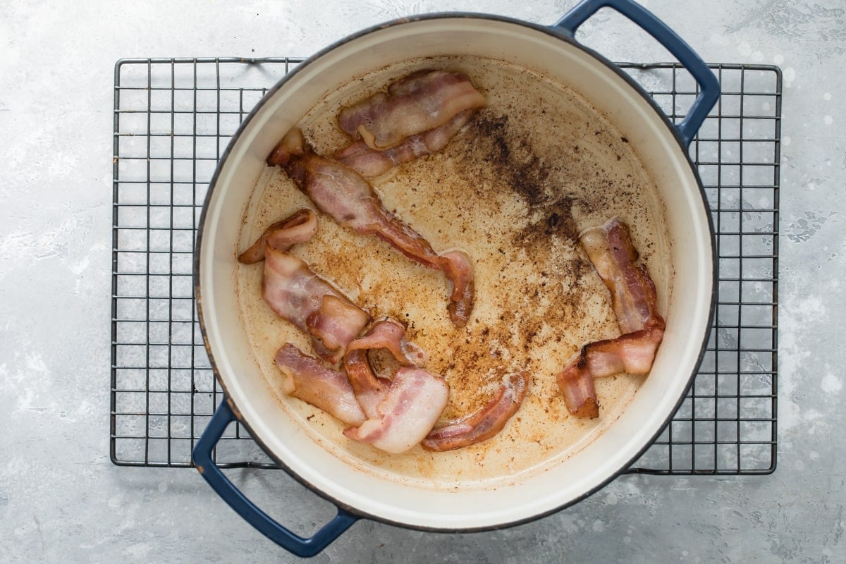 Bacon cooking in the bottom of a dutch oven.